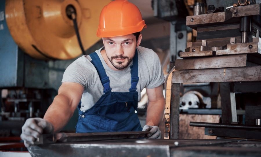 Dekorativna slika: mlad kovinar z oranžno zaščitno čelado med svojim delom v delavnici