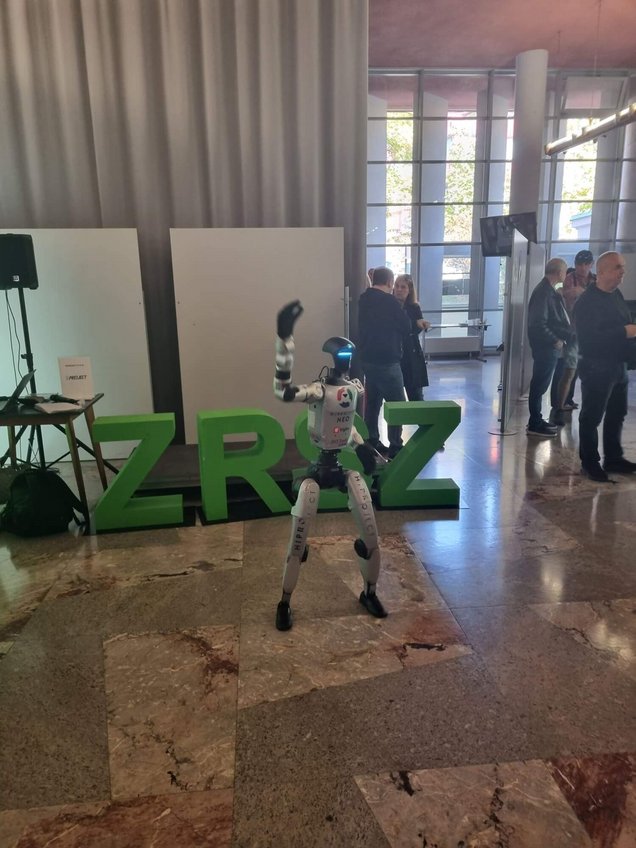 Robot med sprehodom in poplesavanjem na prizorišču Zasavskega zaposlitveno-kariernega sejma 7. oktobra 2026 v Delavskem domu Trbovlje, v organizaciji Zavoda Republike Slovenije za zaposlovanje, Območne službe Trbovlje. V ozadju velike črke #ZRSZ.