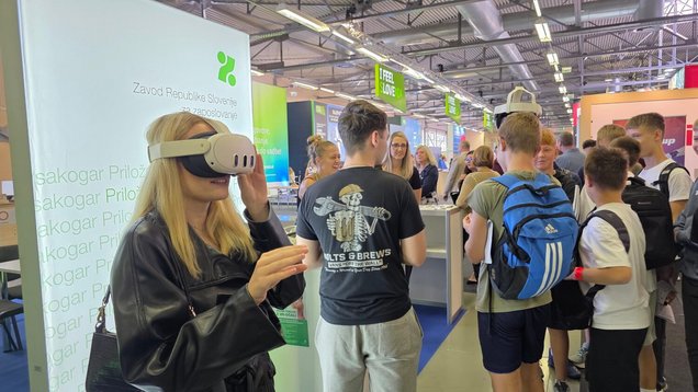 Obiskovalka razstavnega prostora Zavoda Republike Slovenije za zaposlovanje med uporabo VR-očal za promocijo deficitarnih poklicev na 58. Mednarodnem obrtnem sejmu MOS 16. septembra v Celju, v ozadju šolarji, ki so obiskali razstavni prostor.