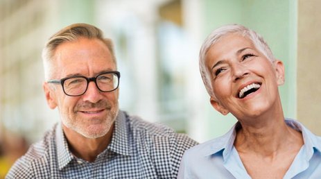 Dekorativna slika za spodbudo za zaposlitev starejših prejemnikov denarnega nadomestila za brezposelnost: nasmejana obraza moškega in ženske v poznih zrelih letih.