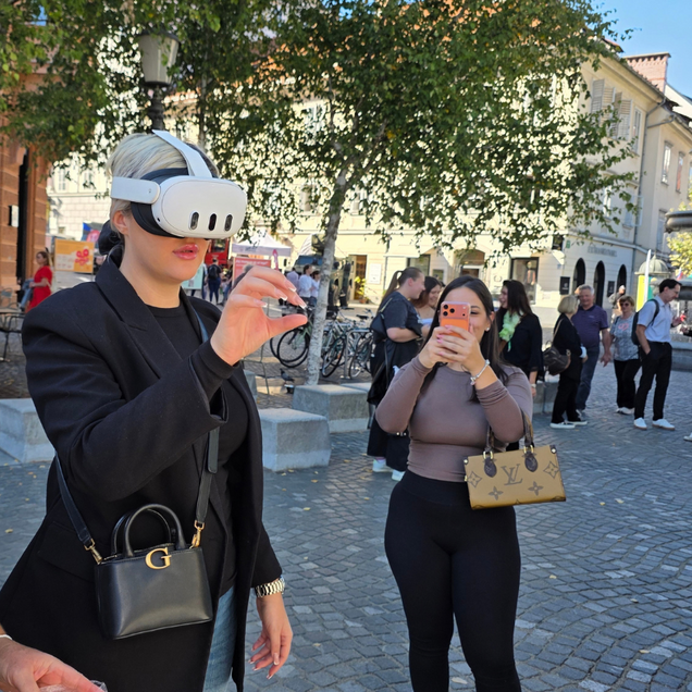 Dogodek Ulica priložnosti - obiskovalka dogodka uporablja VR-očala, druga obiskovalka jo fotografira s pametnim telefonom