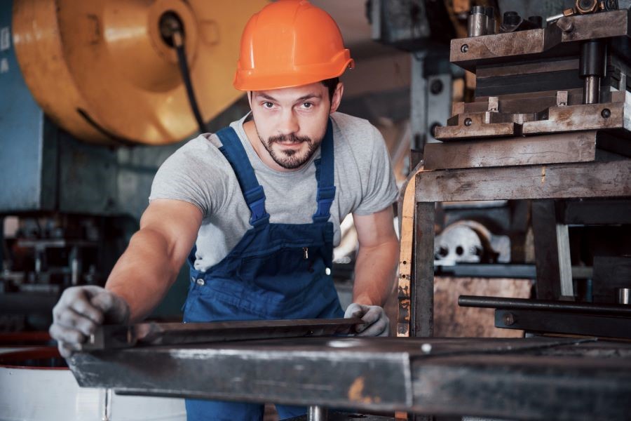 Dekorativna slika: mlad kovinar z oranžno zaščitno čelado med svojim delom v delavnici